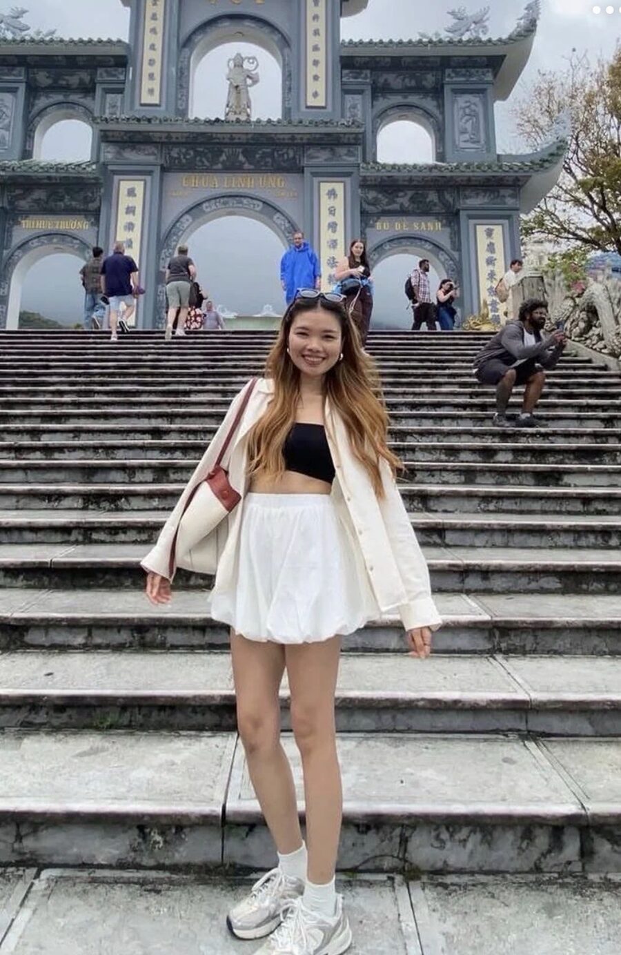 Inney smiling on temple steps with sunglasses on her head and her big bag on her shoulder